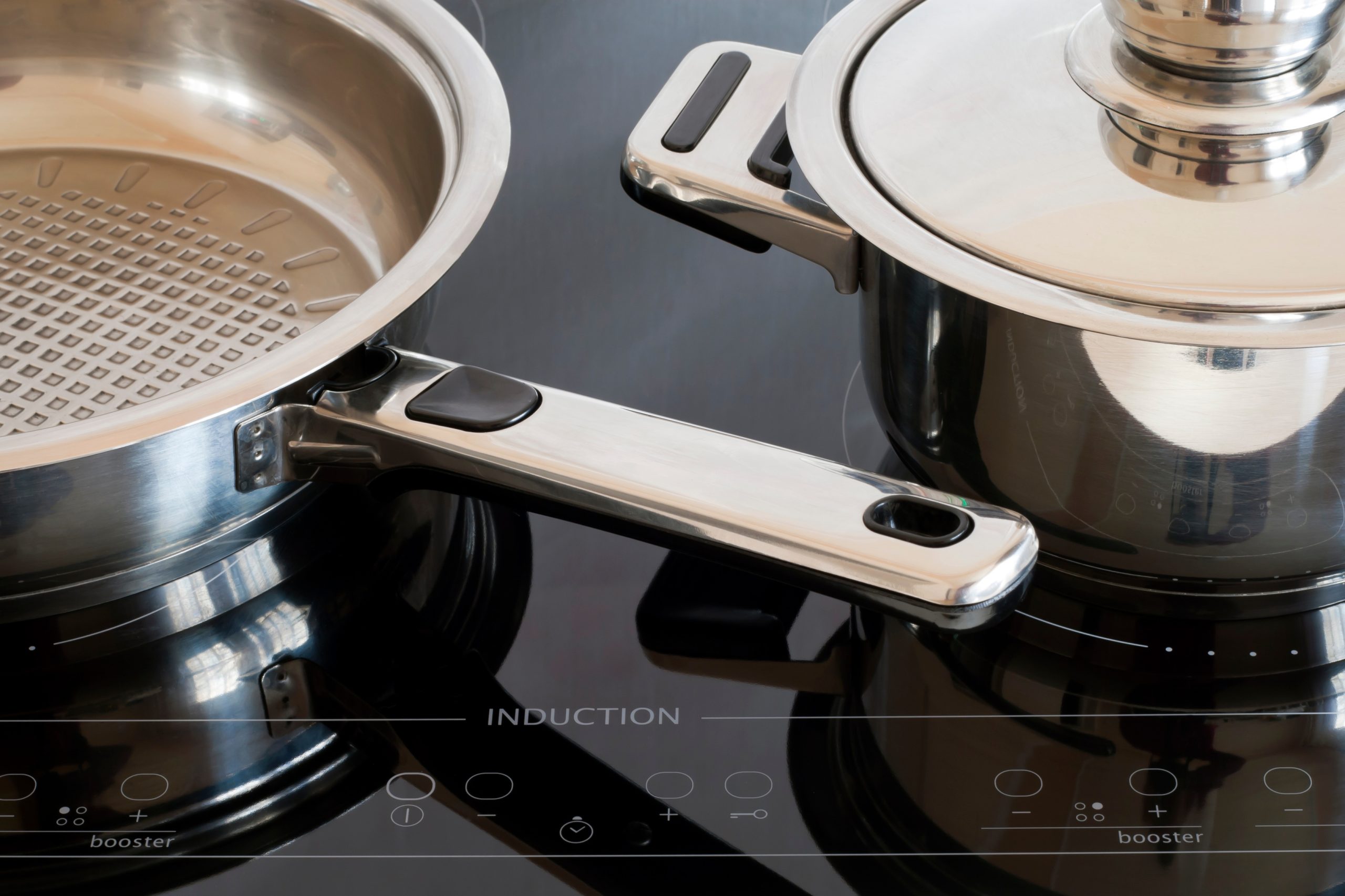 Two stainless steel pots one with a lid sit on a black induction cooktopa sleek setup reflecting 2026 trends in modern kitchens The cooktop panel displays various touch controls and the word induction in the center