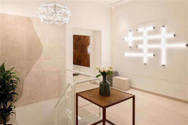 A modern minimalistic interior features a small wooden table with a vase of white flowers geometric wall lights a potted plant and neutral toned walls illuminated by contemporary pendant lighting A modern minimalistic interior features a small wooden table with a vase of white flowers geometric wall lights a potted plant and neutral toned walls illuminated by contemporary pendant lighting Abitzai project | in the heart of rome a space where matter becomes design