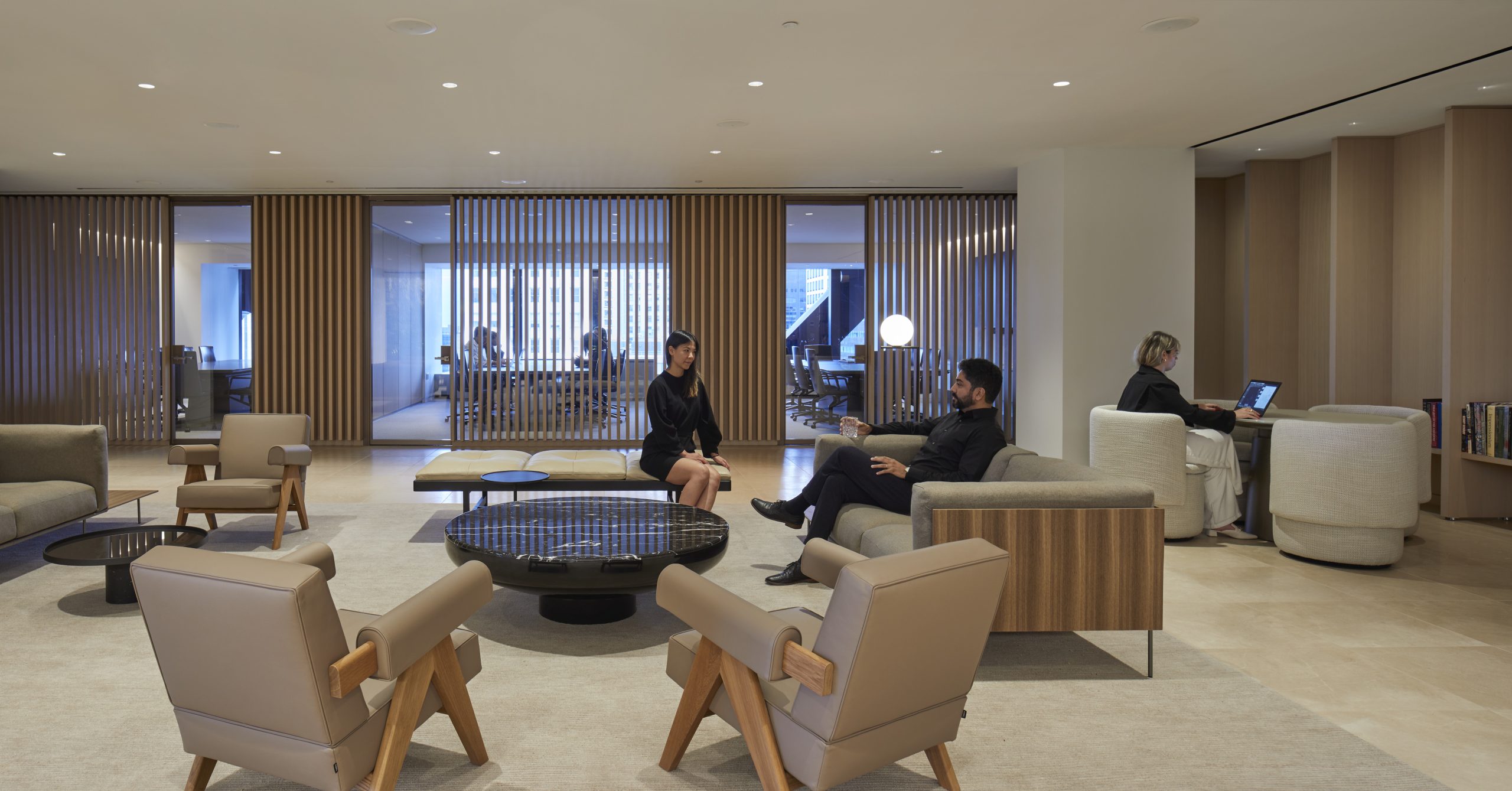 Modern office lounge with neutral furnishings Three people are visible two sitting and talking on a sofa and one working on a laptop in the background Floor to ceiling glass panels divide the space Modern office lounge with neutral furnishings Three people are visible two sitting and talking on a sofa and one working on a laptop in the background Floor to ceiling glass panels divide the space Lighting big ideas with small fixtures from usai lord abbett hello nori & 9 w 57th