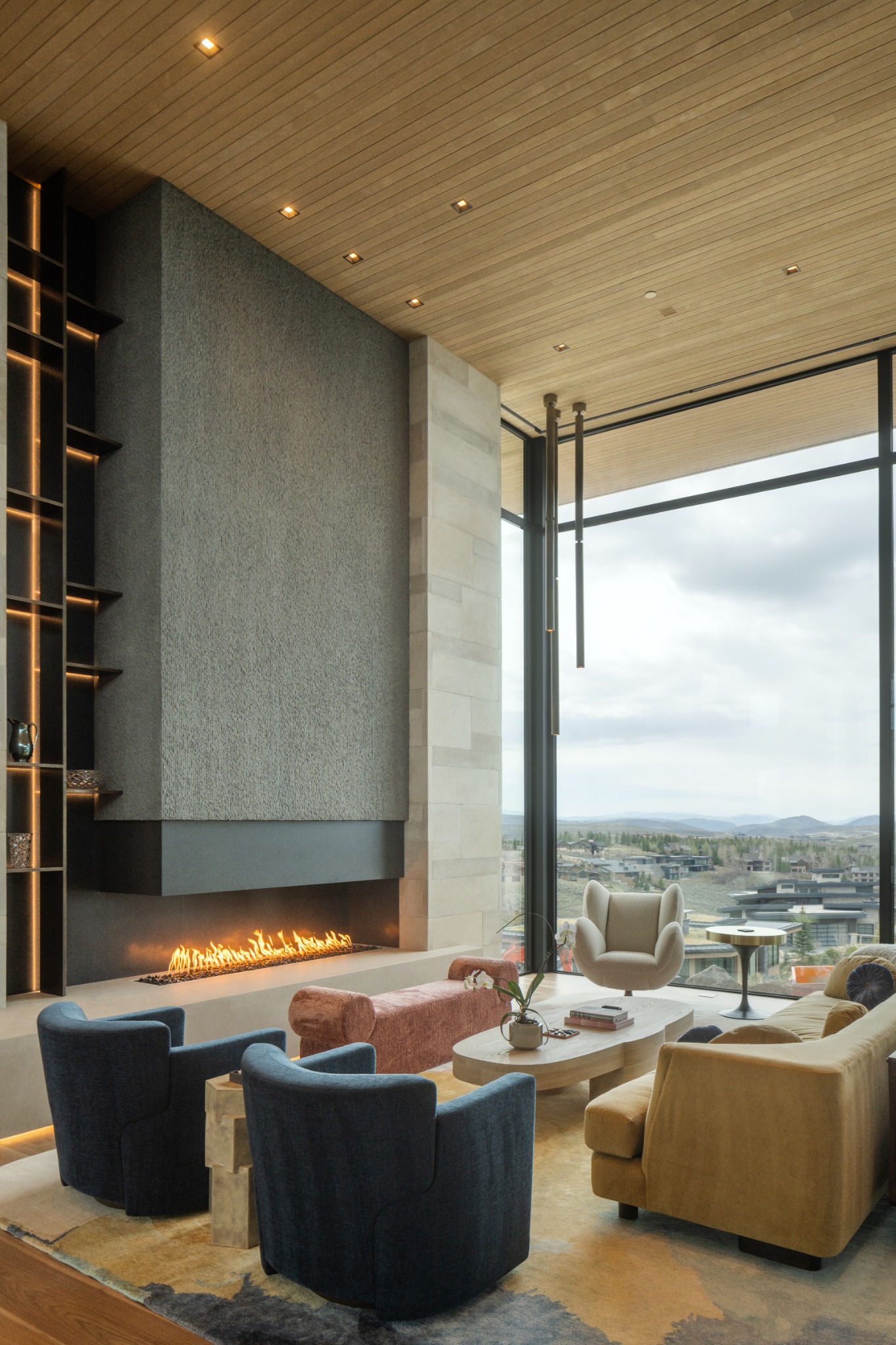 Modern living room with large windows city view fireplace blue and tan armchairs light wood ceiling built in shelving and decorative accents creating a cozy and sophisticated atmosphere 2026 technology designer magazine performance home award winners